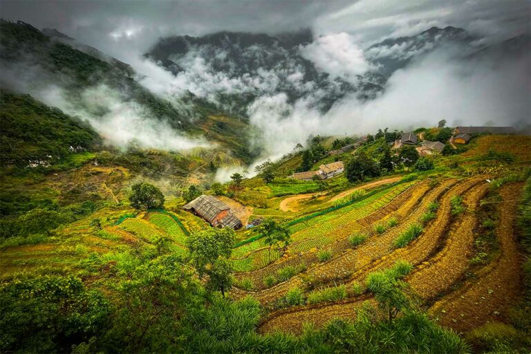 Rijstterrassen en bergdorp in een mistige vallei langs de Ha Giang Loop.