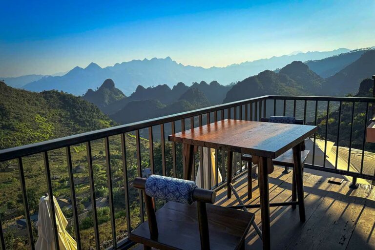 Buiten terras van Ha Giang Aya Lodge met houten tafel en uitzicht op de bergtoppen van de Ha Giang Loop.