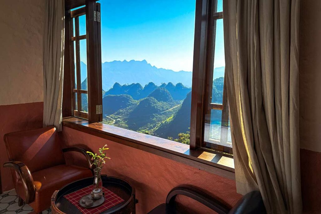 Gezellige zithoek in Ha Giang Aya Lodge met open raam en direct uitzicht op het karstgebergte van Ha Giang.