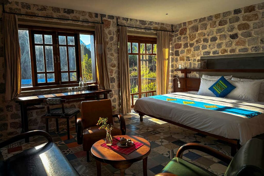 Ruime kamer in Ha Giang Aya Lodge met stenen muren, groot bed en uitzicht op het berglandschap van Ha Giang.