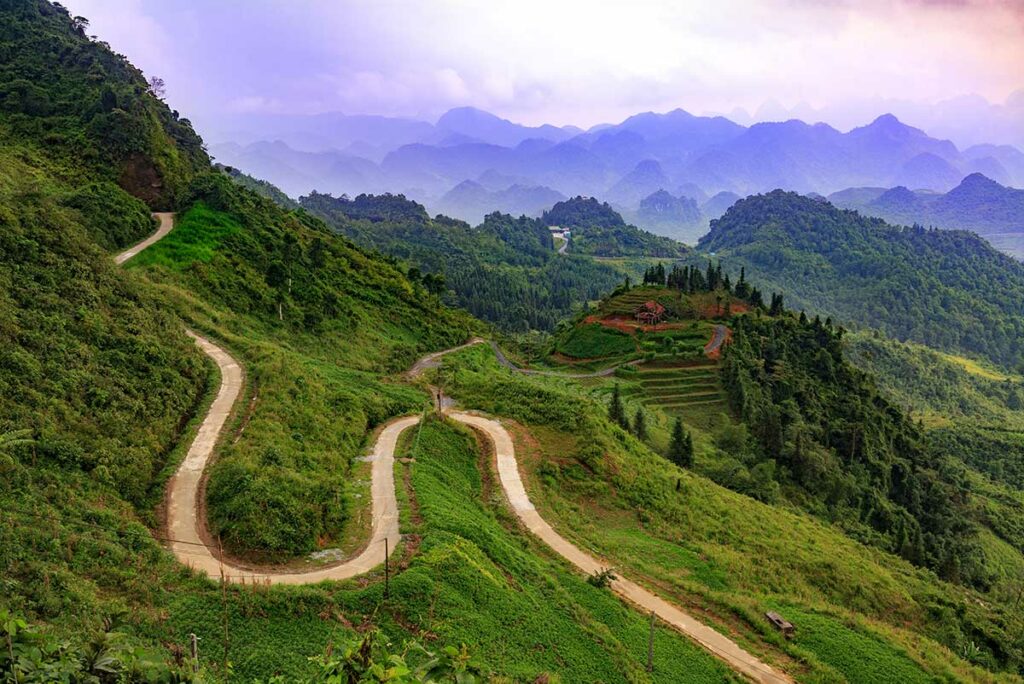 Slingerende weg van de Quan Ba Pass met groene bergen en terrassen in de mistige verte.