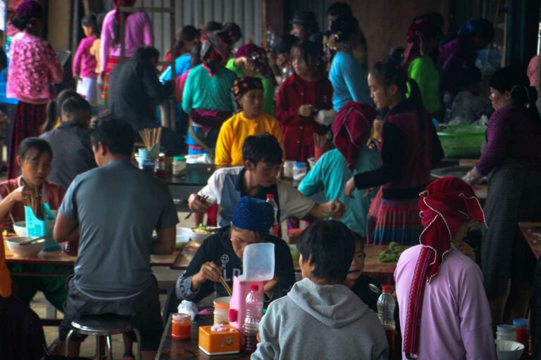 Eetgedeelte op de Sung Trai-markt waar locals in kleurrijke kleding samen noodles eten.