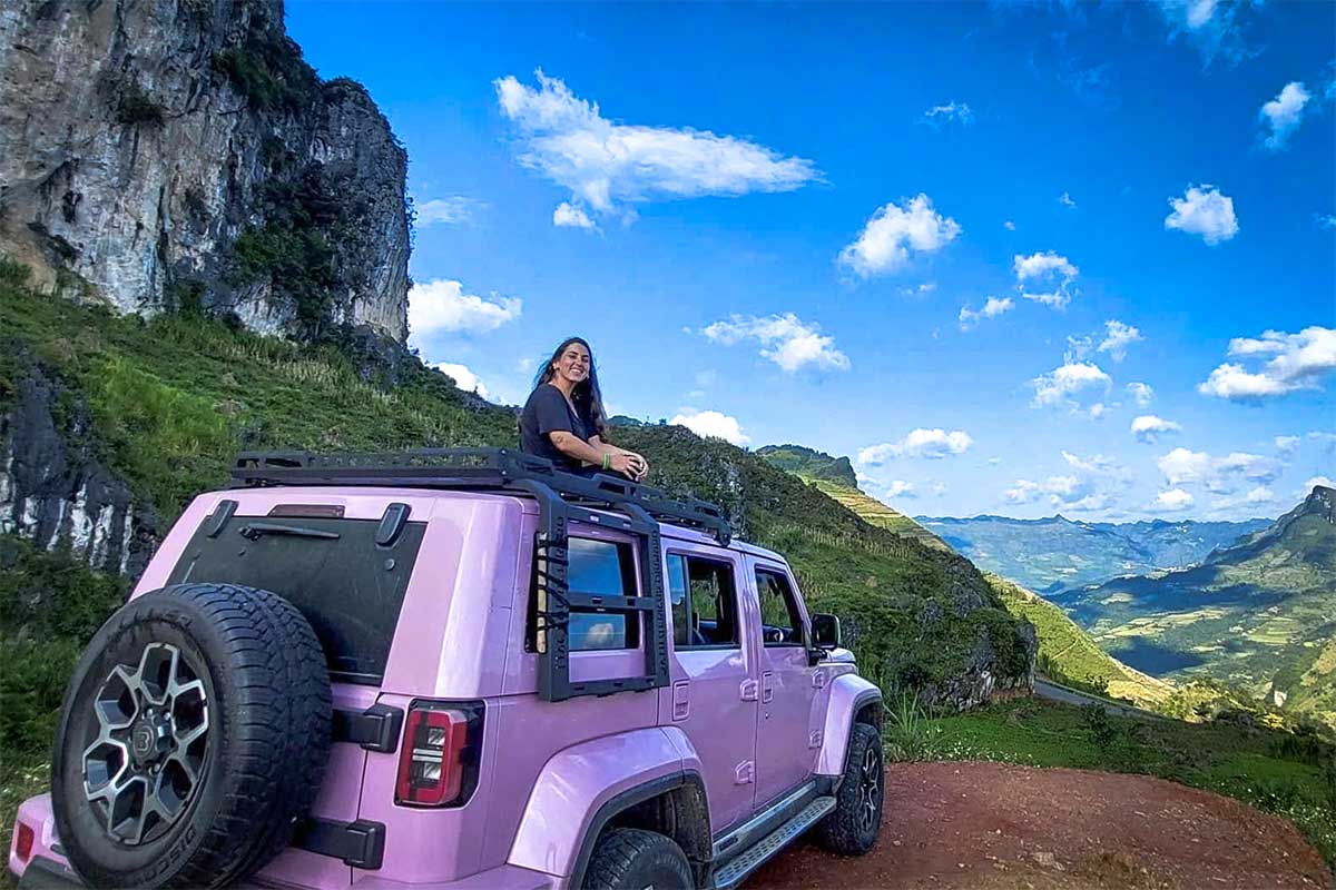 Reiziger zit bovenop een roze jeep tijdens een Ha Giang Loop jeep tour met panoramisch uitzicht over de bergvallei.