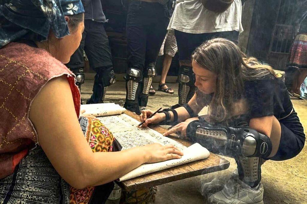 Een reiziger ontmoet lokale etnische bewoners tijdens de Ha Giang Loop groepstour, terwijl ze samen traditionele patronen tekenen op handgemaakt papier.
