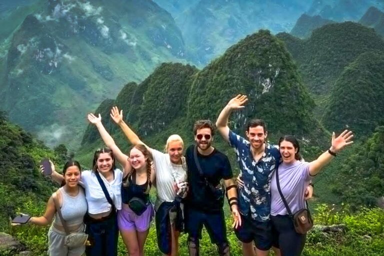 Grote groep jonge reizigers bij een panoramisch uitzichtpunt in Ha Giang, omringd door groene bergen.