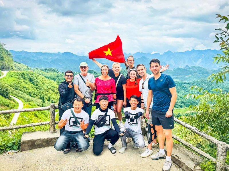 Nederlandse en Belgische reizigers tijdens een Ha Giang Loop Easy Rider tour poseren als groep bij een spectaculair uitzichtpunt met Local Vietnam-gidsen en de iconische bergen op de achtergrond.