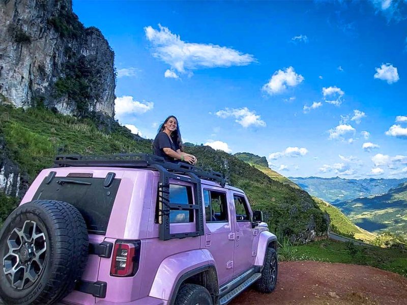 Reiziger zit bovenop een roze jeep tijdens een Ha Giang Loop jeep tour met panoramisch uitzicht over de bergvallei.