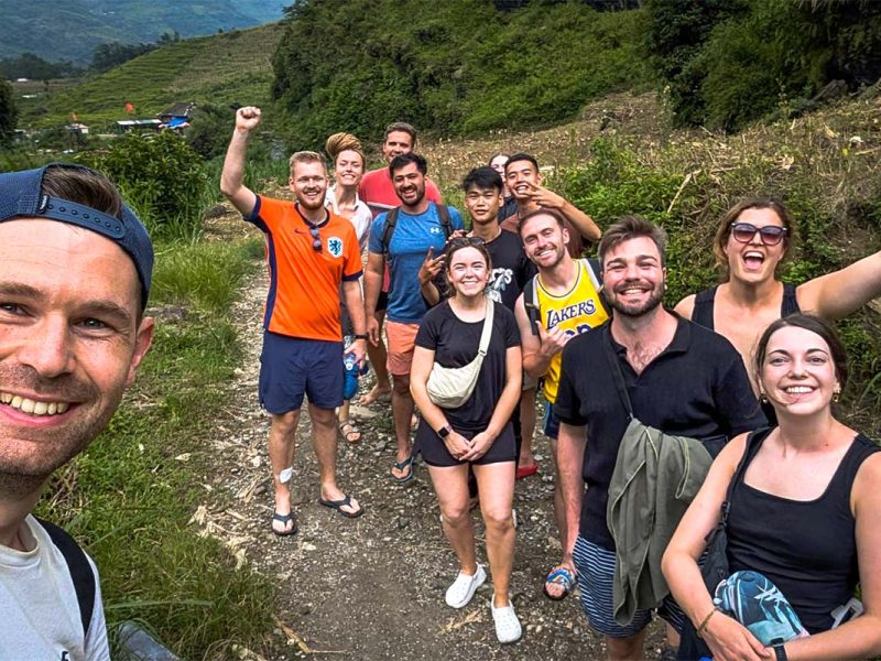 Een groep Nederlanders geniet van hun Ha Giang Loop tour tijdens een wandeling door het berglandschap, met veel enthousiasme en groene terrassen op de achtergrond.