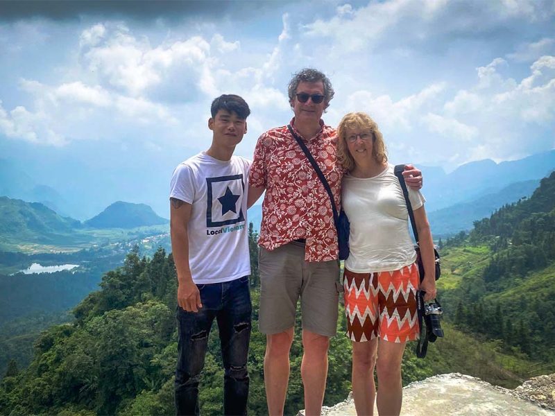Nederlandse reizigers staan met hun lokale gids op een uitkijkpunt tijdens een Ha Giang Loop tour, met een weids panorama van valleien en bergtoppen achter hen.